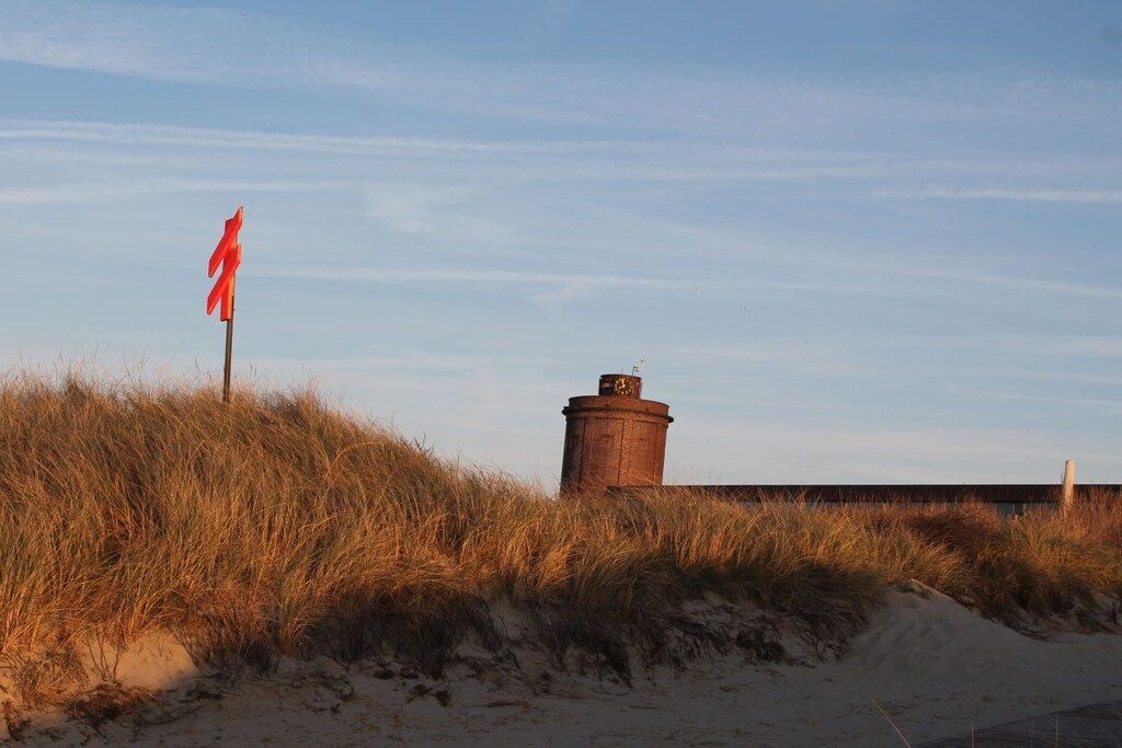 A sandy landscape with a red flag and a cylindrical structure.