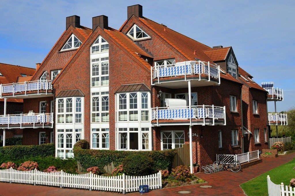 A multi-story brick building with balconies, large windows, and a white picket fence.