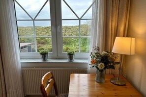 Ett rum med utsikt över naturen genom ett stort fönster, ett träbord, en stol, en lampa och en vas med blommor.