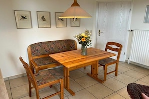 A dining area with a wooden table, two chairs, a bench, and a lamp. - Holiday apartment in Juist with swimming pool (Juist)