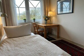 A bedroom with a bed, a desk, a chair, a window with curtains, a lamp, and a framed picture on the wall. - Holiday apartment in Juist with swimming pool (Juist)