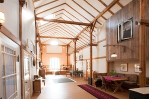 A spacious interior with a high ceiling, wooden beams, a dining area, and a living space with a fireplace.