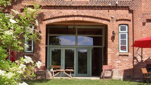 Ein Backsteinhaus mit großem Bogenportal, Außenplätzen und einem roten Sonnenschirm.