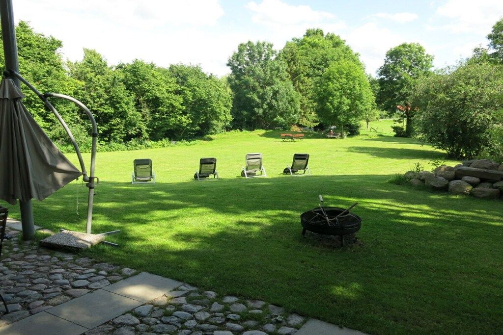 A well-maintained lawn with four lounge chairs, a grill, and a pergola structure.