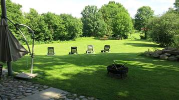 A well-maintained lawn with four lounge chairs, a grill, and a pergola structure.