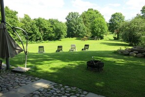 A well-maintained lawn with four lounge chairs, a grill, and a pergola structure.
