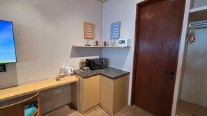 Una cocina compacta con microondas, cafetera y un estante pequeño con objetos decorativos.