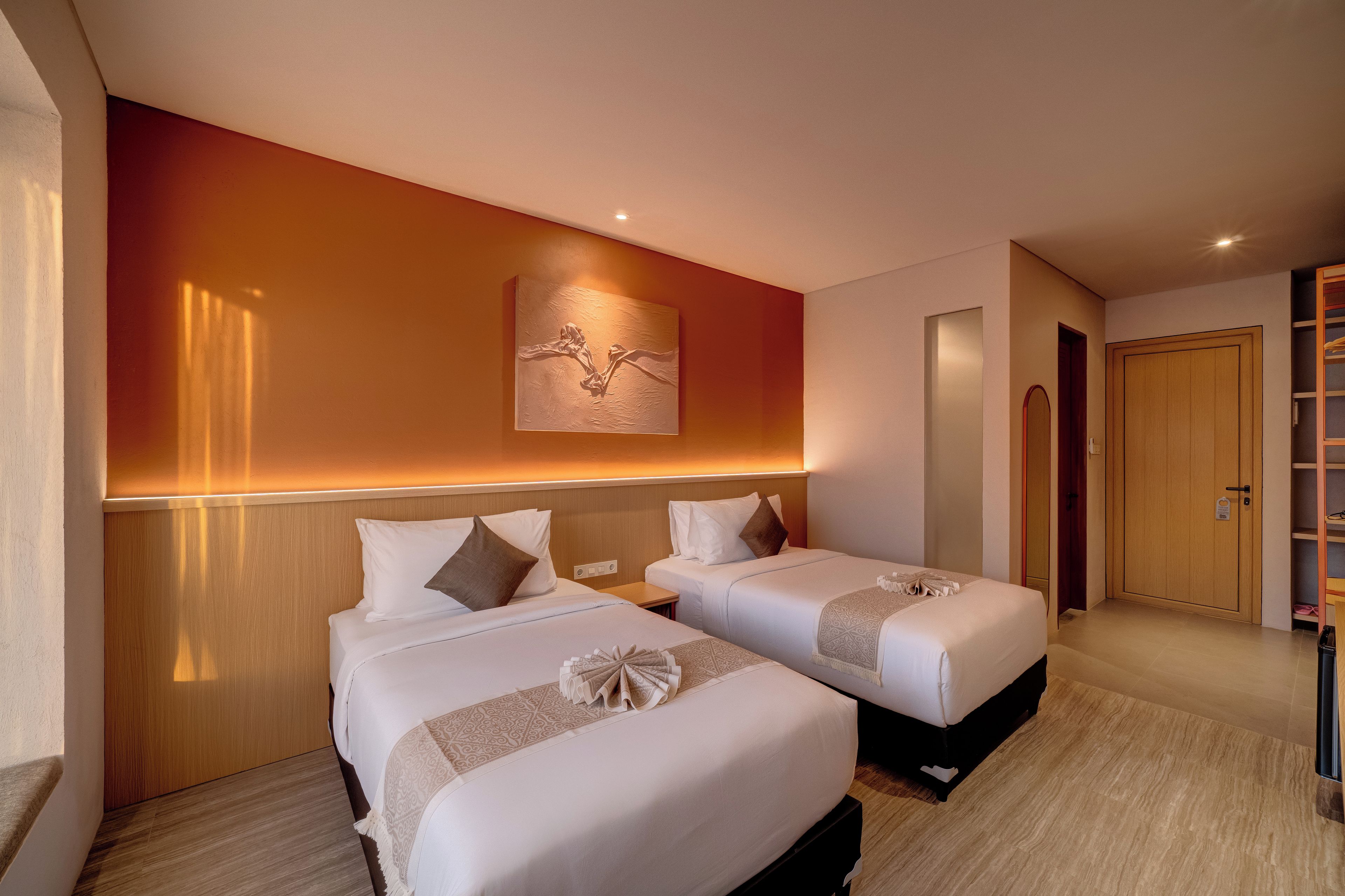 Habitación de hotel con dos camas, cabecera de madera, una obra de arte colgada en la pared y una puerta que da a un armario.