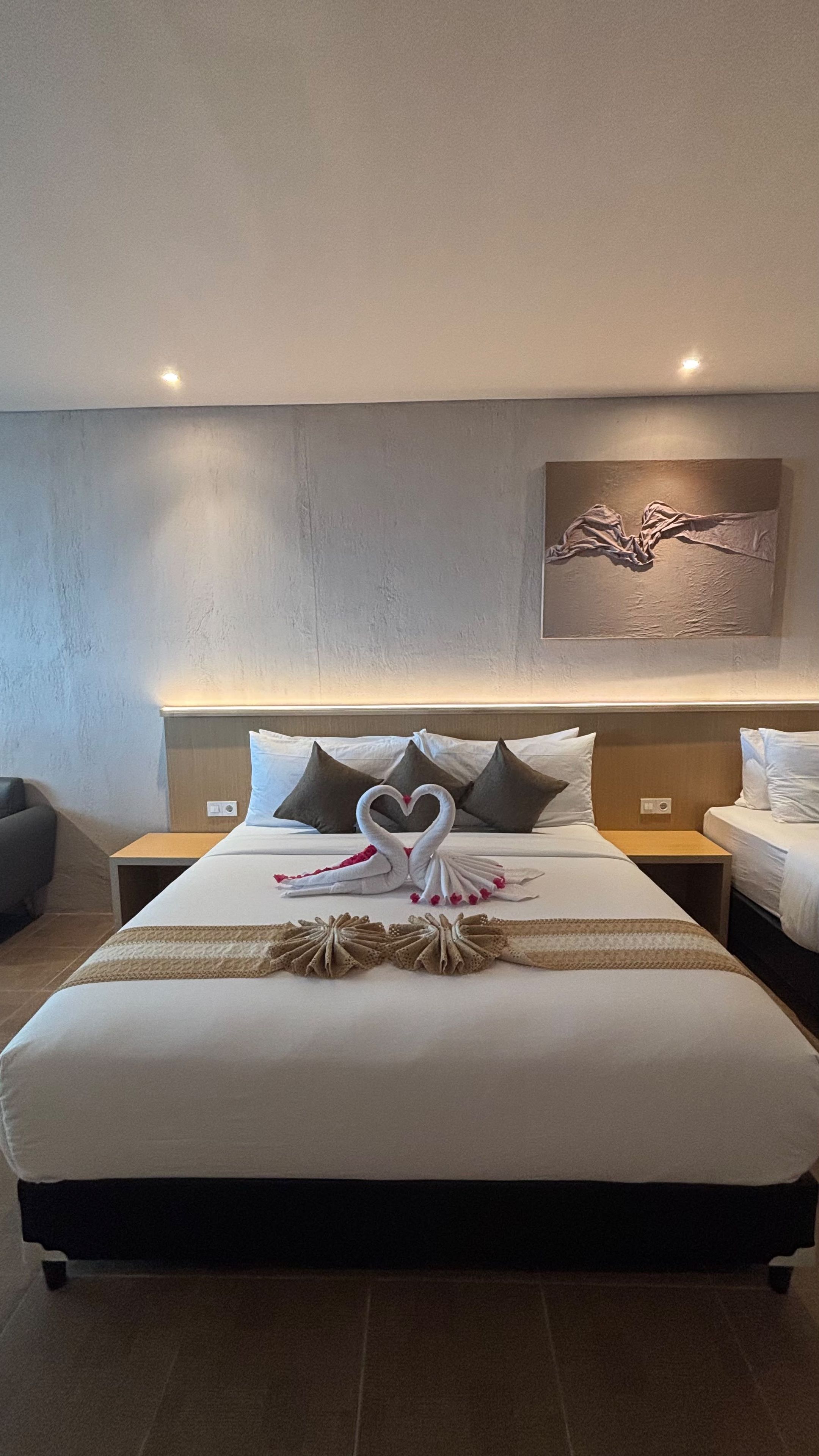 Habitación de hotel con una cama grande, cabecera con lámpara, obra de arte en la pared y mesita de noche con lámpara.
