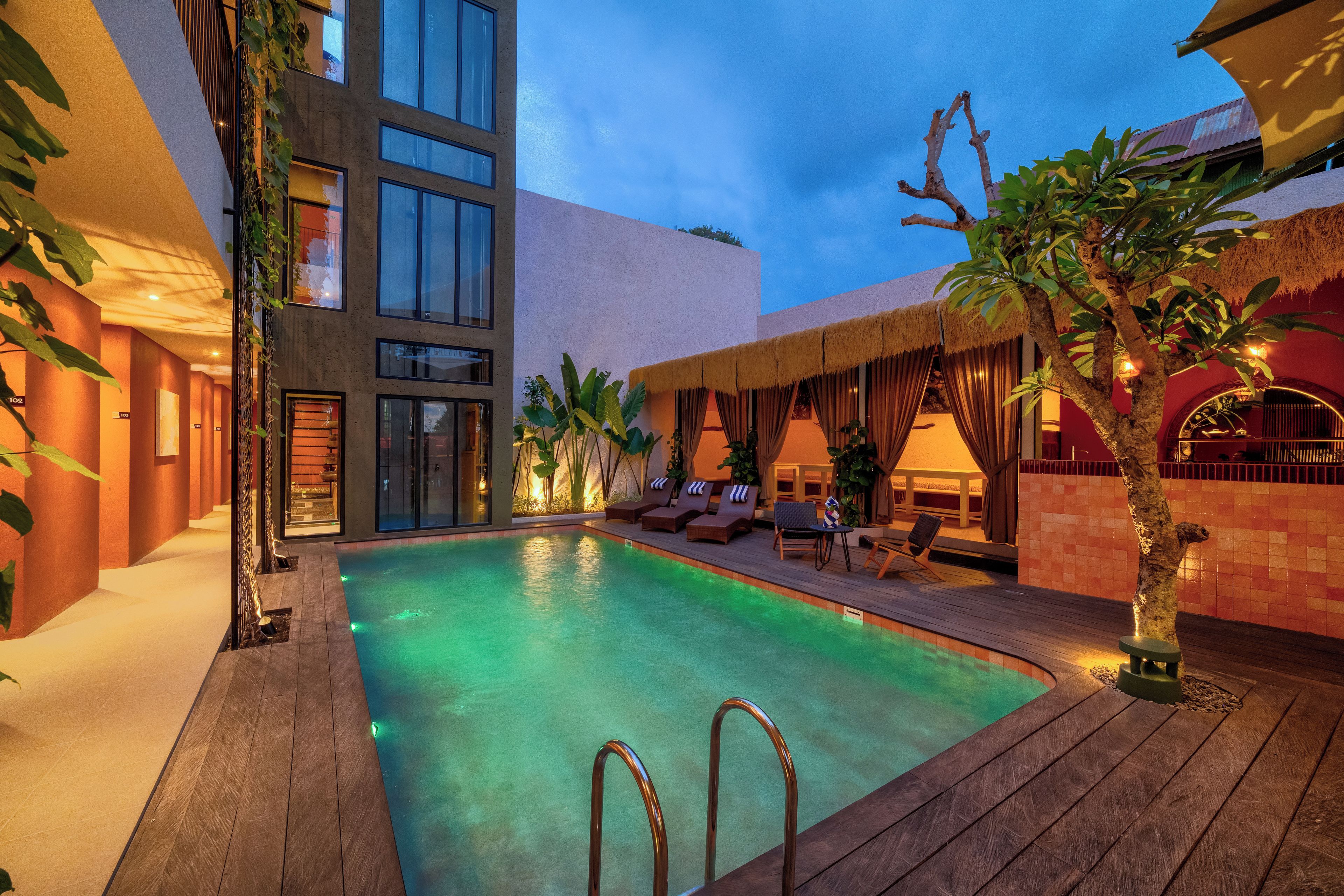 A swimming pool area with a wooden deck, lounge chairs, and a building with multiple windows.