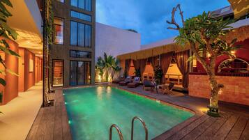 A swimming pool area with a wooden deck, lounge chairs, and a building with multiple windows.