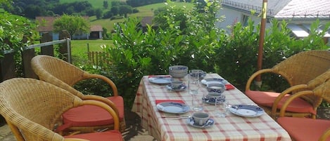 An outdoor dining area with wicker chairs and a table set for four, overlooking a rural landscape.