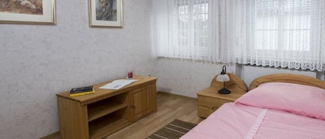 A bedroom with a bed, a wooden nightstand, a desk, and two framed pictures on the wall.