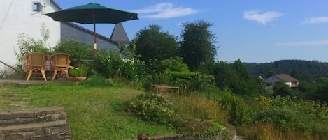Een wit gebouw met een stenen muur, terras en een groene parasol.