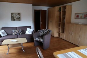 A living room with a sofa, armchair, wooden cabinet, and a table. - Holiday apartment with 2 bedrooms (Ellenz-Poltersdorf 1)
