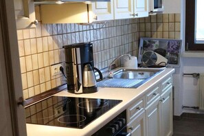 Eine Küche mit einem schwarzen Induktionskochfeld, einer Kaffeemaschine, einem Spülbecken und einer gefliesten Spritzschutzwand.