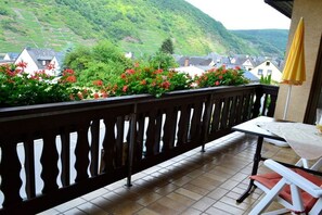 Ein Balkon mit Blick auf eine Hügel Landschaft, ein Tisch mit einem Stuhl und ein gelber Sonnenschirm.