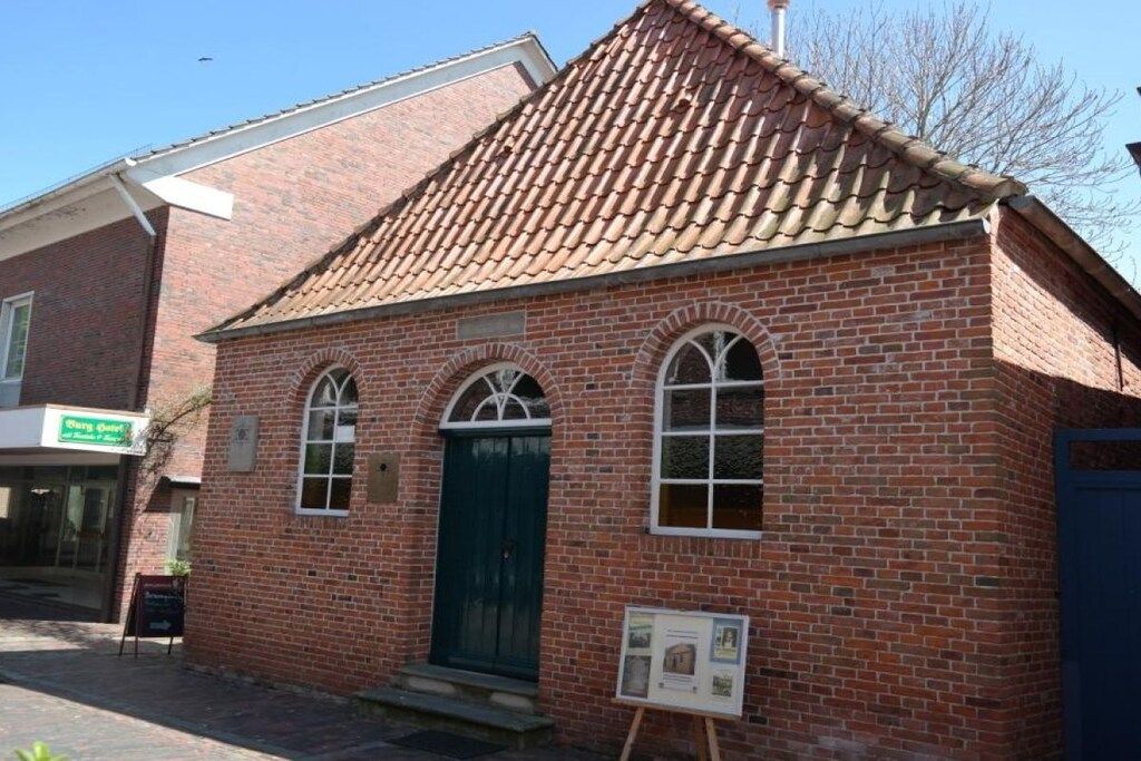 A brick building with a tiled roof, a green door, and arched windows.