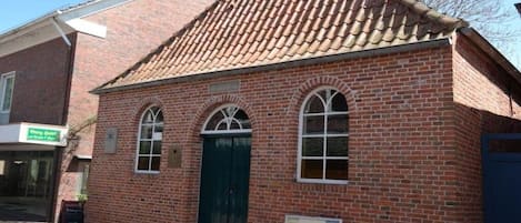 A brick building with a tiled roof, a green door, and arched windows.