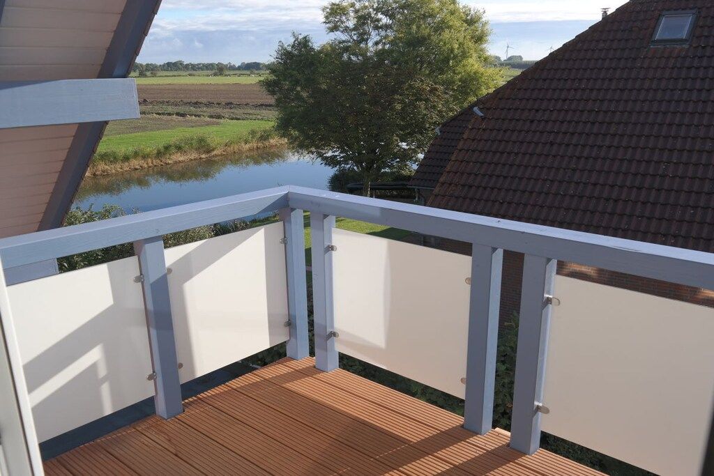 A wooden deck with a white railing overlooking a river and fields.