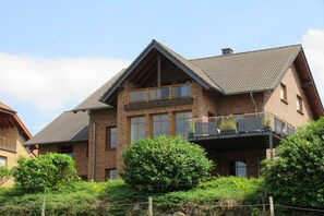 Ein zweistöckiges Haus mit Balkon, Ziegelaußenwand und geneigtem Dach.