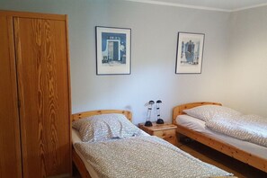 Ein Zimmer mit zwei Einzelbetten, einem Holzschrank und zwei gerahmten Bildern an der Wand.
