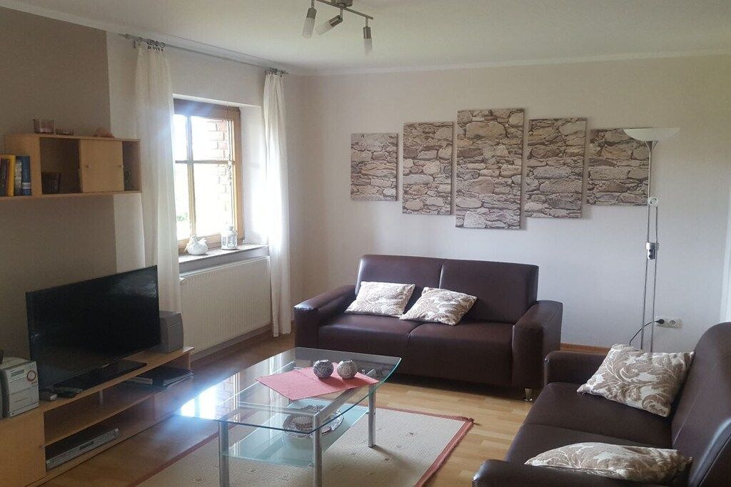 A living room with a sofa, a glass coffee table, a television, and stone wall art.