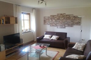 A living room with a sofa, a glass coffee table, a television, and stone wall art. - Holiday apartment in Daun with swimming pool (Daun)