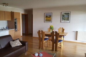 A modern kitchen with wooden cabinets, a dining area with a table and chairs, and a living room with a sofa. - Holiday apartment in Daun with swimming pool (Daun)