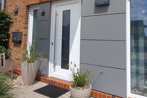 A modern building with a white door, a grey wall, and two large potted plants on the ground. - Holiday apartment with 1 bedroom (Carolinensiel)