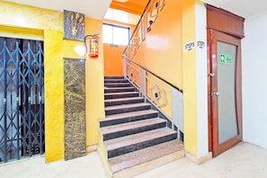 A staircase with a handrail, a fire exit sign, and a door with a fire exit sign. - Townhouse Oak SR Nagar Metro Station (Hyderabad)