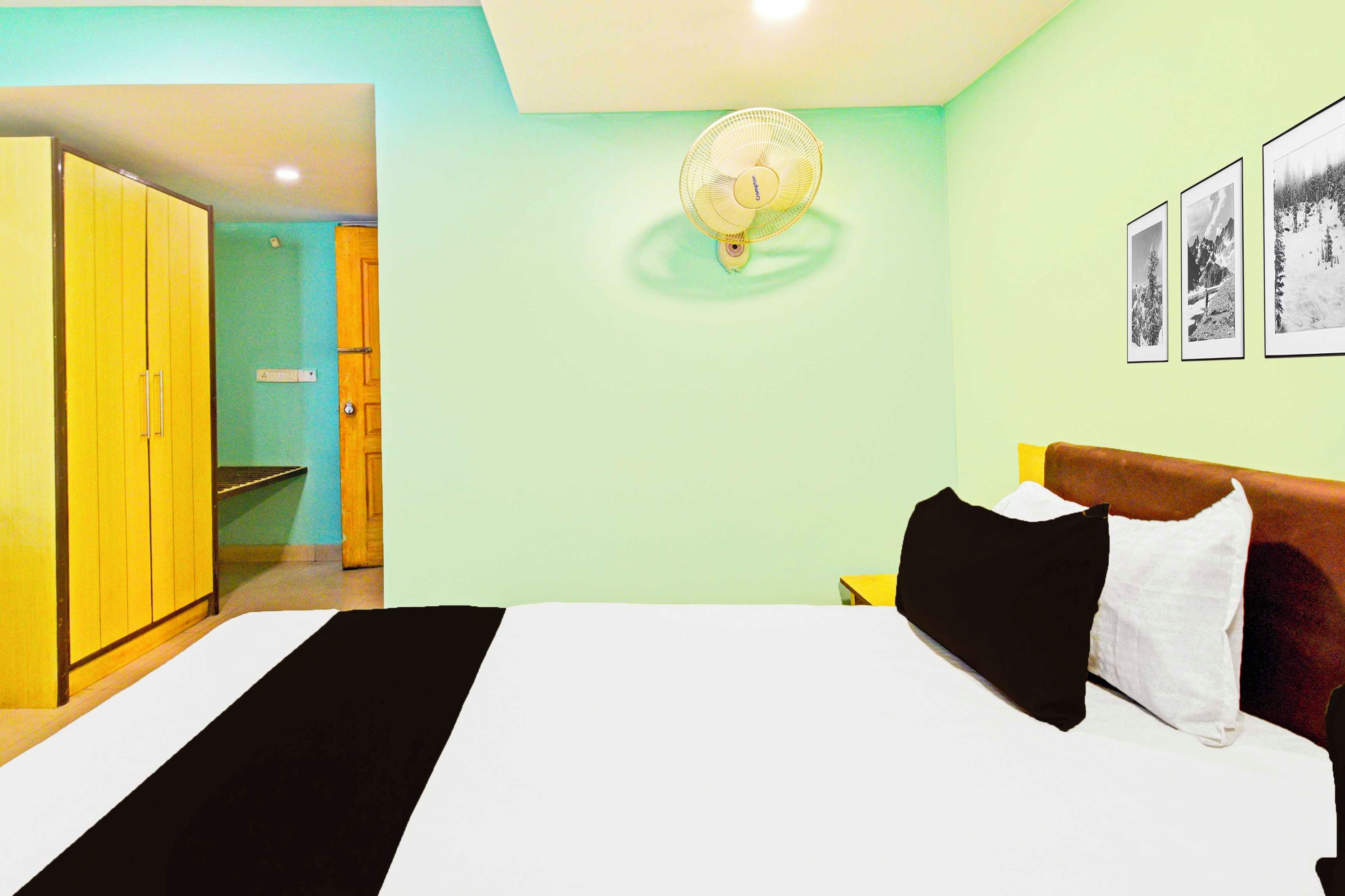 Quarto de hotel com cama, mesa de cabeceira, luminária na parede e porta para o banheiro.