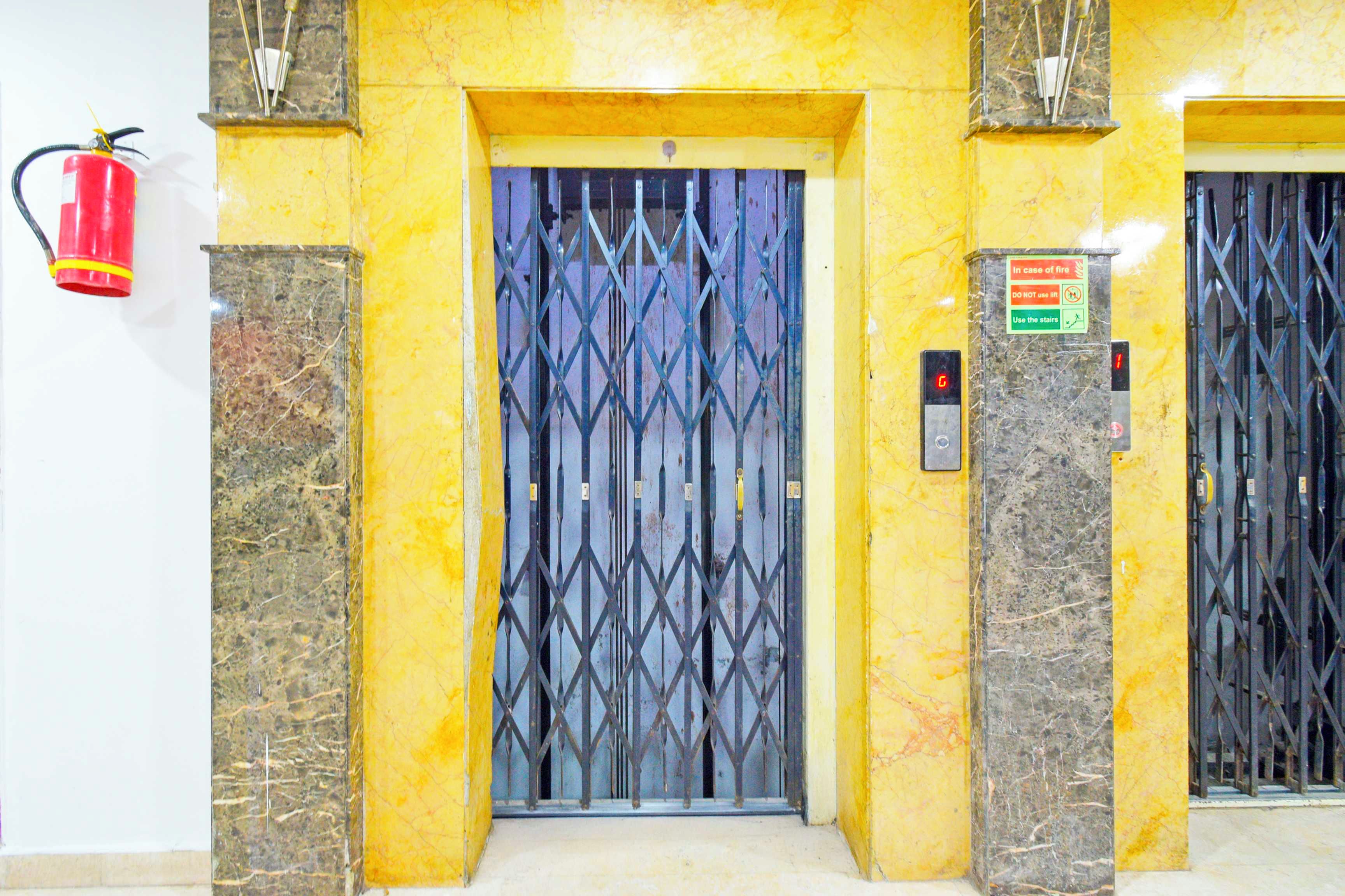 Un ascensor con una puerta metálica, un extintor instalado en la pared y un cartel que indica 'En caso de incendio' con instrucciones.