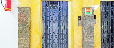 Un ascensor con una puerta metálica, un extintor instalado en la pared y un cartel que indica 'En caso de incendio' con instrucciones.