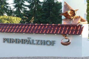 Ein Gebäude mit einem Schild, auf dem 'PUMPALZHOF' steht, und einer kupferfarbenen Skulptur einer Figur mit Hut.