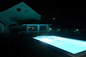 En pool i månskenet med ett hus i bakgrunden.