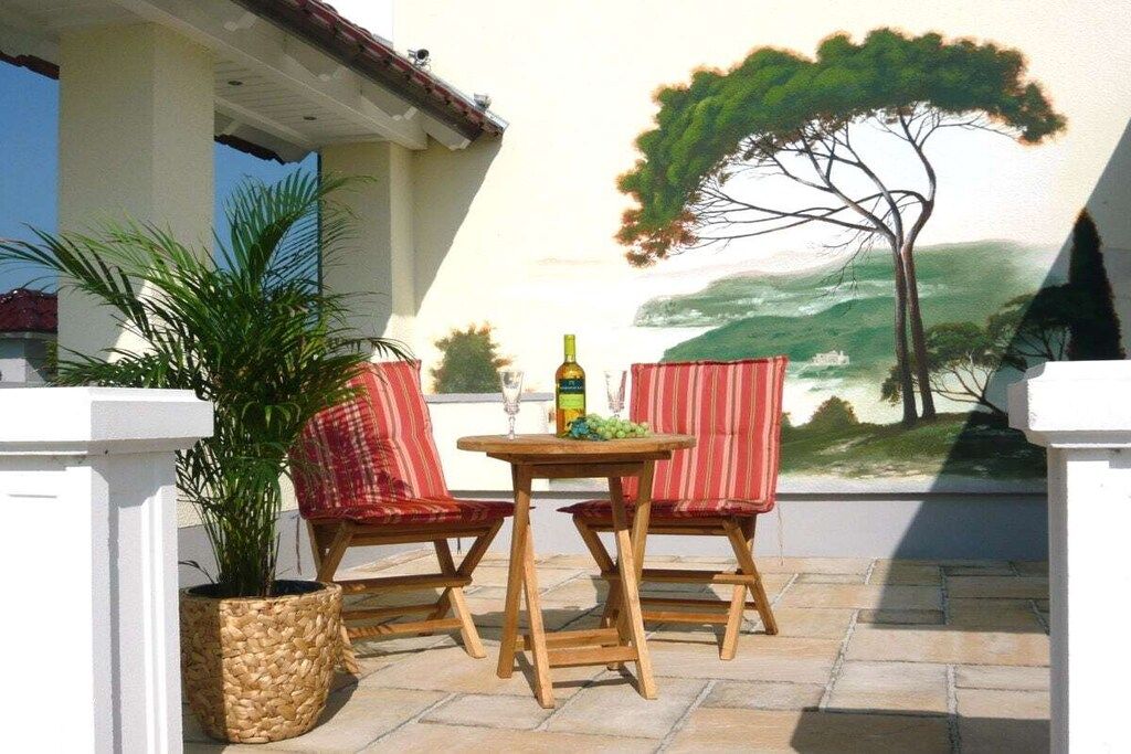 An outdoor patio with two wicker chairs, a small round table, and a potted plant.