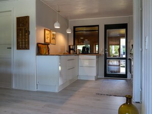 Una cocina moderna con armarios blancos, iluminación colgante y vistas al comedor.
