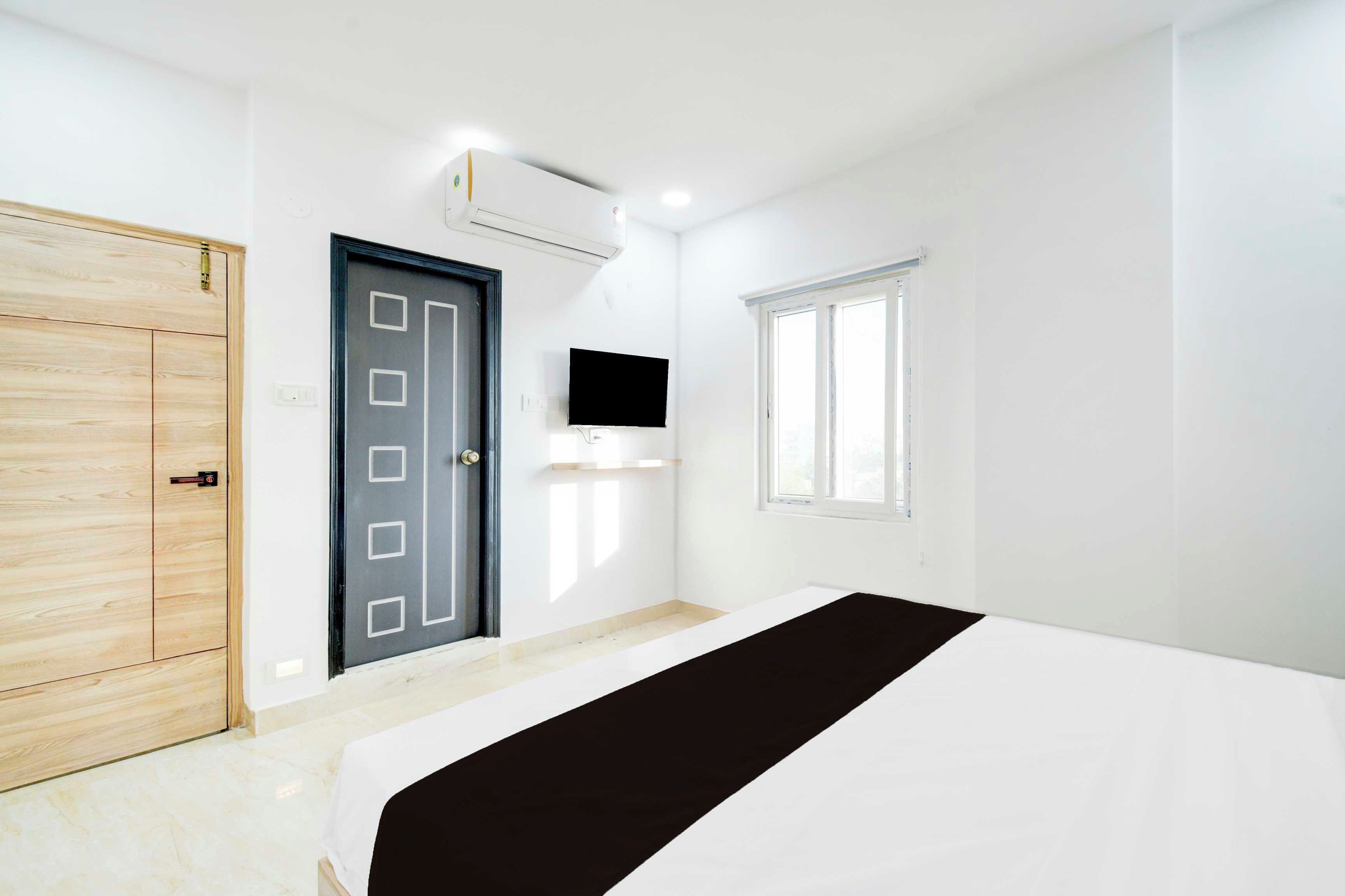 Een slaapkamer met een bed, een kledingkast, een deur, een aan de muur bevestigde televisie en een raam.