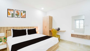 A modern bedroom with a bed, a wardrobe, a bedside table with a lamp, and a chair. - Townhouse Oak LB Nagar Metro Station (Hyderabad)