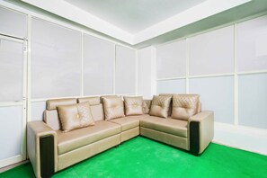 A beige sectional sofa with quilted pillows in a room with white walls and a green carpet. - Townhouse Oak LB Nagar Metro Station (Hyderabad)