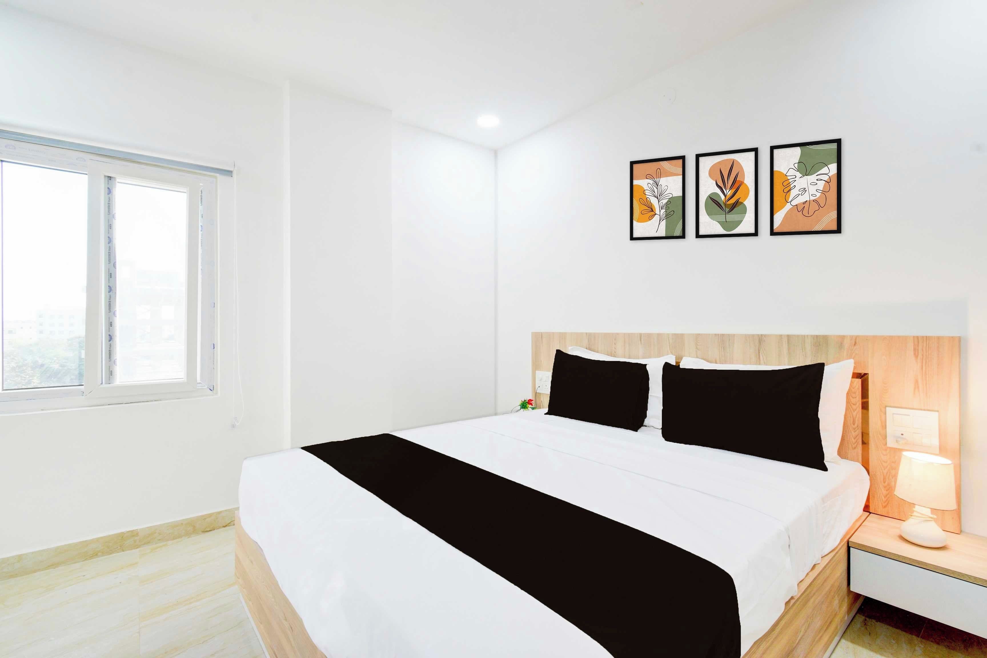 A hotel room with a bed, a nightstand, a lamp, and three framed artworks on the wall.