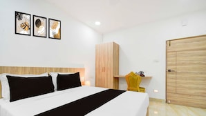 A hotel room with a bed, a wooden wardrobe, a yellow chair, and artwork on the wall. - Townhouse Oak LB Nagar Metro Station (Hyderabad)