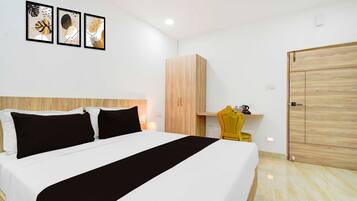 A hotel room with a bed, a wooden wardrobe, a yellow chair, and artwork on the wall.
