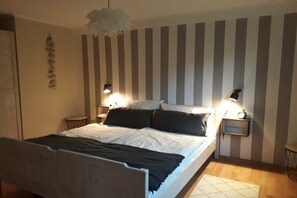 A bedroom with a bed, bedside lamps, a wall-mounted light fixture, and a rug on the floor. - Cog Baltrum in the Captain's House (Neßmersiel - Dornum)