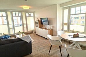Ein modernes Wohnzimmer mit einer Couch, einem Esstisch, Stühlen, einem Fernseher und einem Schrank.