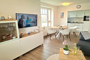 Ein modernes Wohnzimmer mit Fernseher, Essbereich und Küche.