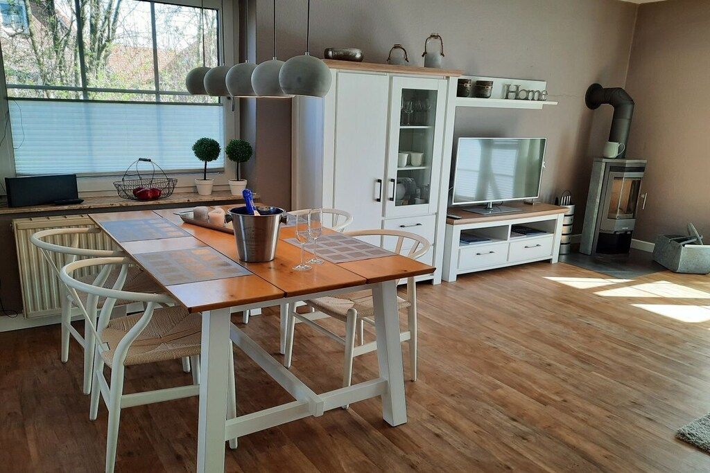 A modern kitchen with a dining table, white chairs, a built-in oven, and a TV.
