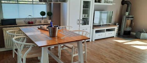 A modern kitchen with a dining table, white chairs, a built-in oven, and a TV.