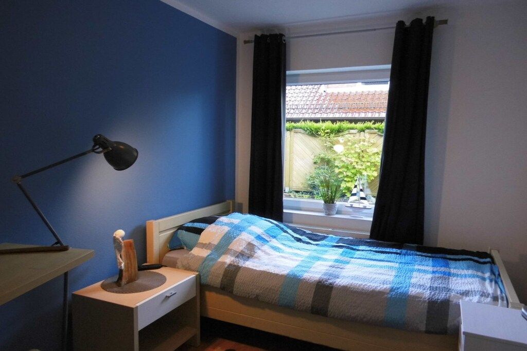 A bedroom with a bed, a bedside table, a lamp, and a window with curtains.